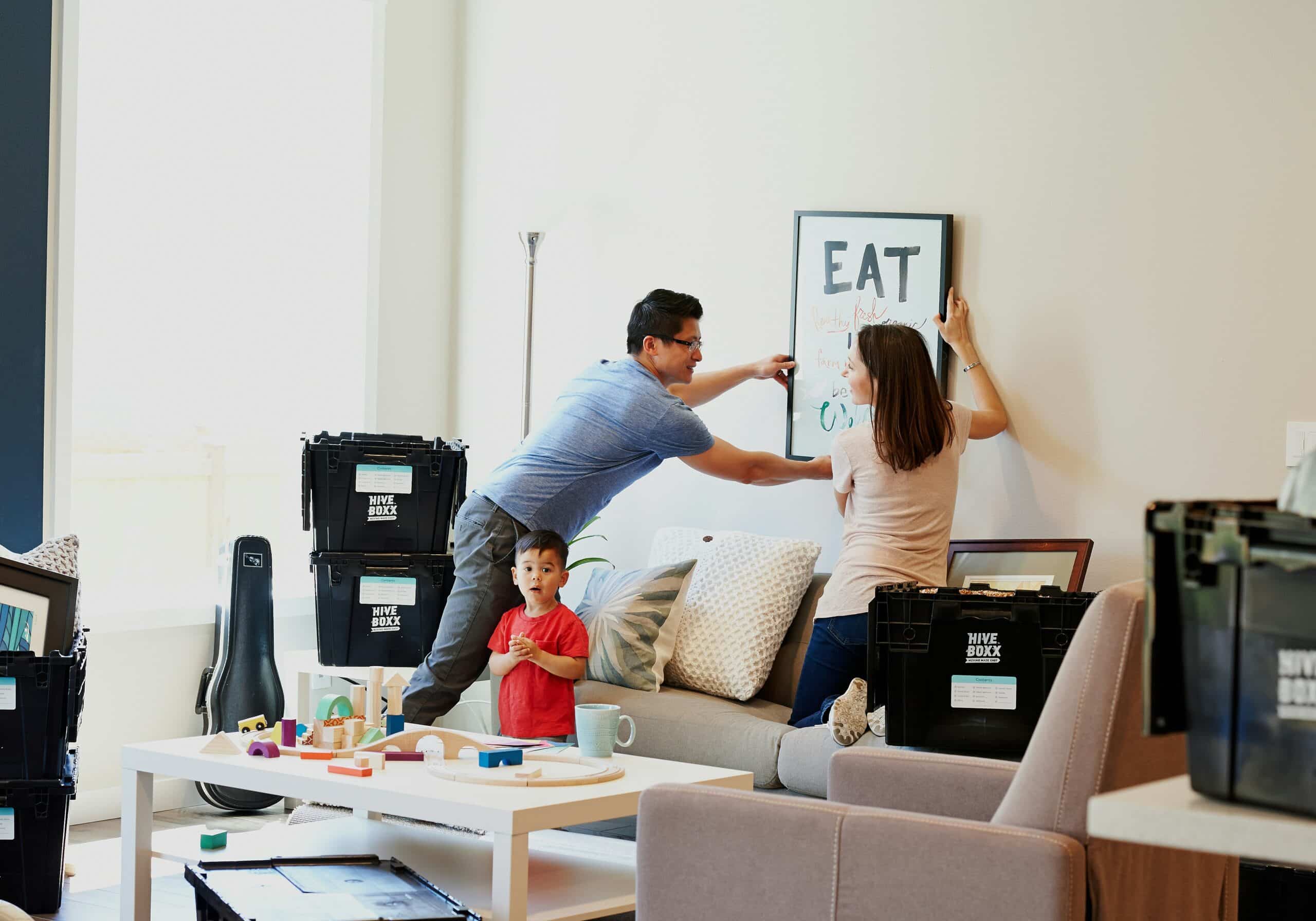 Couple putting up frame on wall with moving in boxes around them.