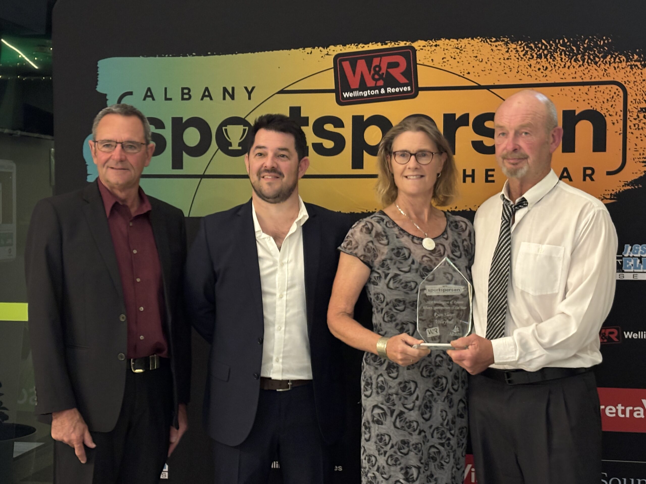 four people standing for a photo in front of a banner for Albany Sports Person of The Year.